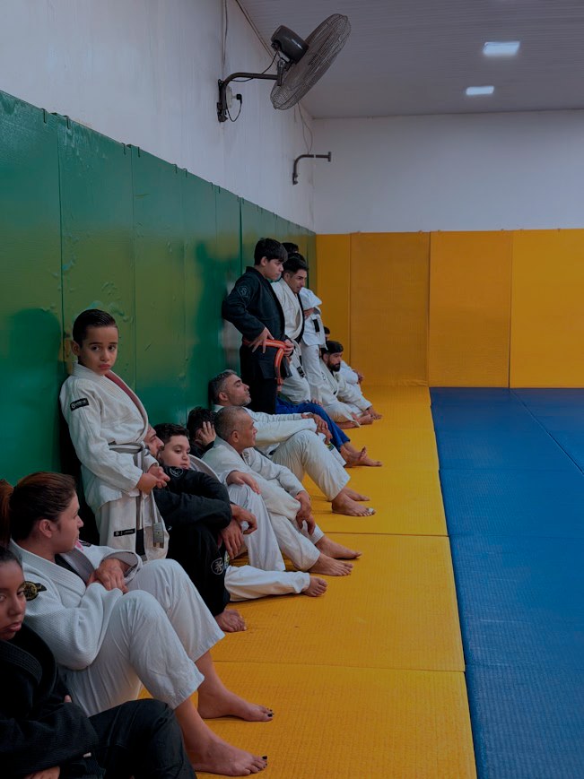 Alunos de kimono sentados no tatame durante o treino